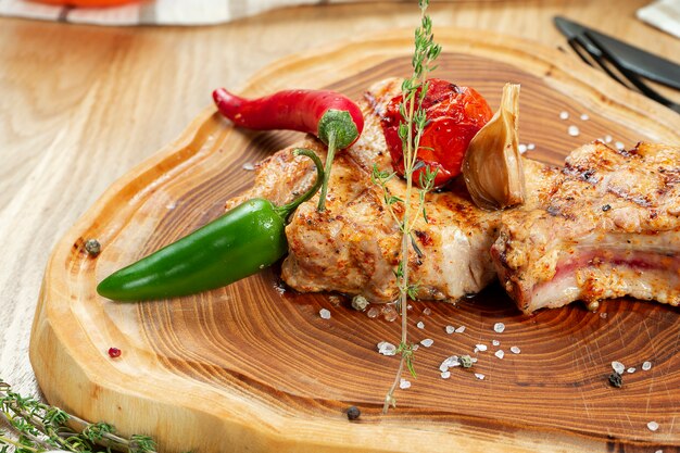 Braciola di maiale alla griglia con peperoncino e pomodoro su una tavola di legno. Avvicinamento. Messa a fuoco selettiva