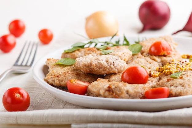 Braciole di maiale fritte con i pomodori e le erbe su un piatto ceramico bianco