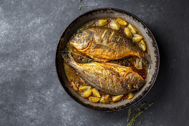 Brama di mare o dorada al forno con cipolla e erbe in padella su sfondo scuro