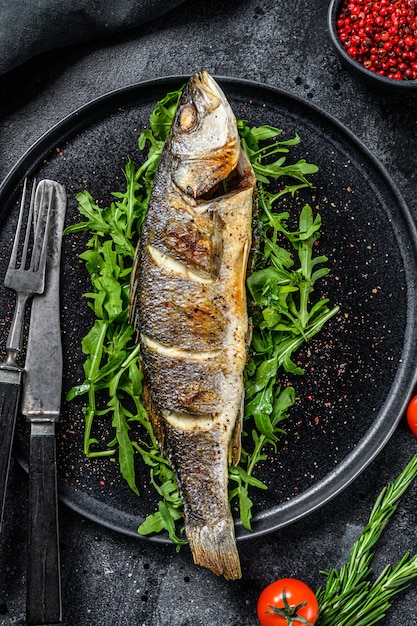 Branzino al forno con rucola sul tavolo nero.