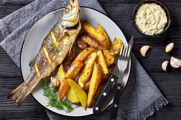 Branzino arrosto su un piatto con patatine fritte