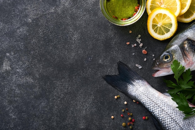 Branzino crudo Pesce di mare fresco Spigola con sale, pepe, prezzemolo, olio d'oliva e limone su fondo rustico in cemento scuro Pesce fresco pronto da cucinare Sfondo di cottura degli alimenti Vista dall'alto dello spazio della copia