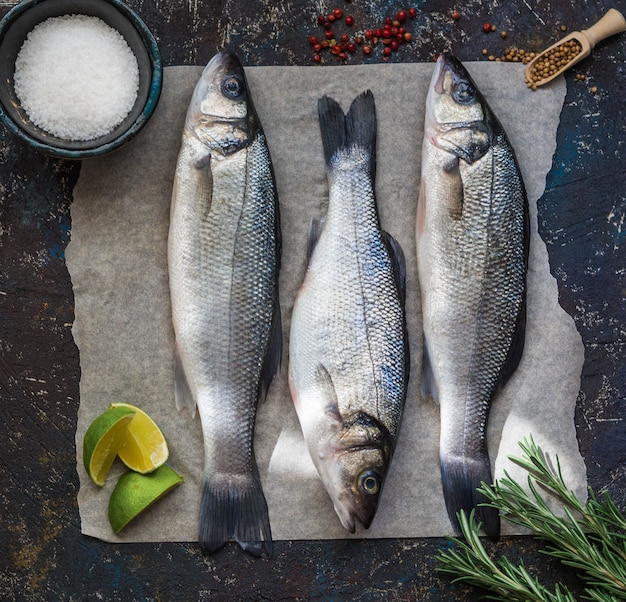 Branzino del pesce crudo tre e altri ingredienti sull'annata scura. Vista dall'alto