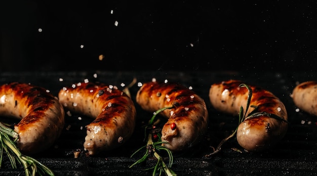 Bratwurst di salsiccia alla griglia che cuociono su una griglia ardente Griglia per barbecue che sfrigola su carboni ardenti. carne alla griglia in acciaio. Formato banner lungo