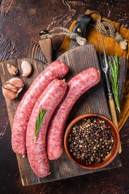 Bratwurst Salsicce di carne cruda su tavola di legno con spezie. Sfondo scuro. Vista dall'alto.