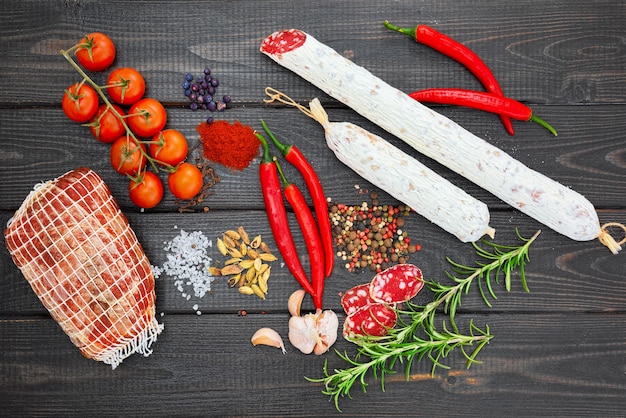 Bresaola e salsiccia affettata con spezie, peperoncino, aglio e pomodori su fondo rustico in legno scuro.