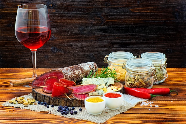 Bresaola stagionata affettata con spezie e un bicchiere di vino rosso su fondo rustico in legno scuro.