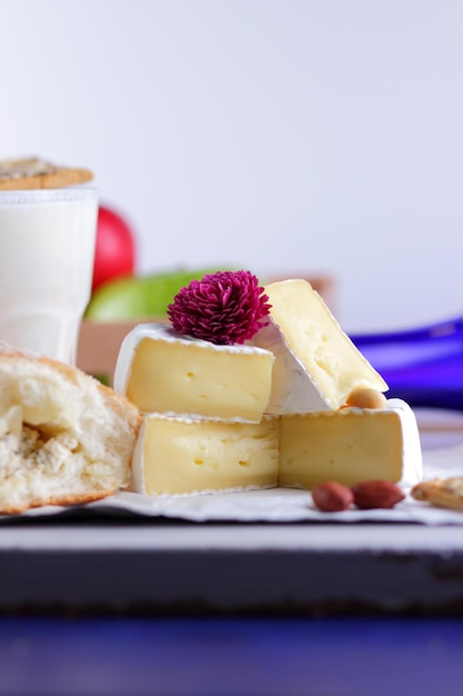 Brie bianco gourmet o formaggio camembert con frutti di bosco miele e noci su una pergamena bianca Natura morta di formaggio frutta e una bottiglia blu su sfondo sfocato Primo piano