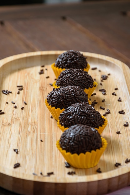 Brigadieri allineati su un piatto di legno. Il focus è sul brigadeiro nel centro.