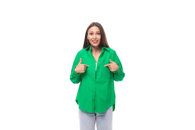 brillante allegra giovane modello femminile dai capelli bruni con occhi marroni in una camicia verde che posa su uno sfondo bianco con spazio di copia