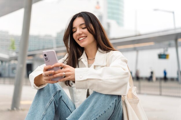 Brillante e allegra giovane donna con shopper sulla spalla in attesa di trasporto pubblico alla stazione sorridente