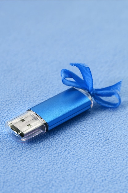 Brillante scheda di memoria flash USB blu con un fiocco blu si trova su una coperta di morbido tessuto felpato blu chiaro