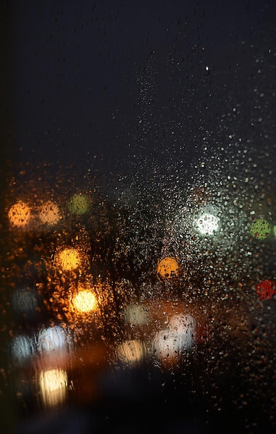 Brillanti città di notte di luci attraverso il vetro delle finestre in gocce di pioggia sfondo astratto luci sfocate