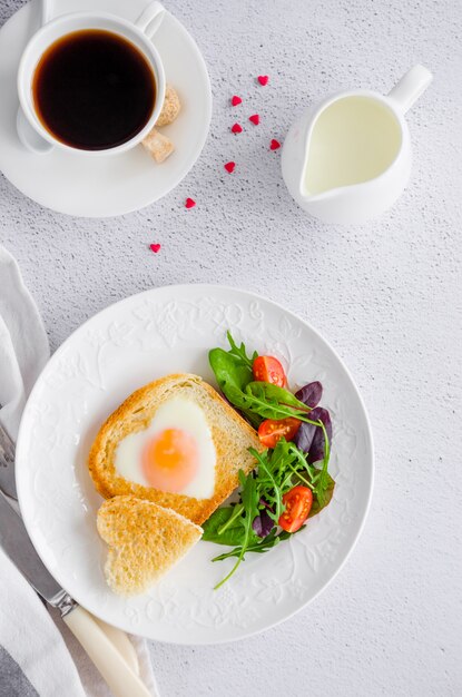 Brindare a forma di cuore con uovo su un piatto bianco con rucola e pomodorini