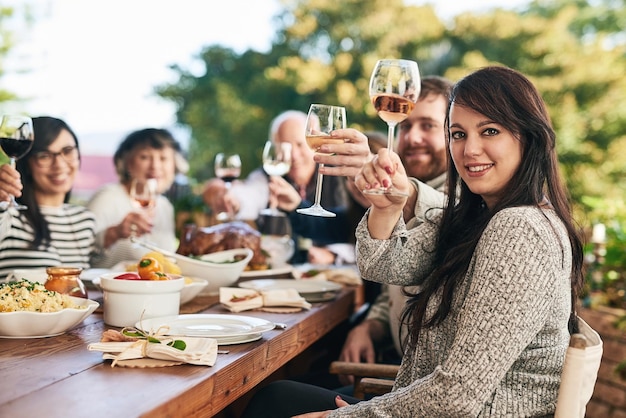 Brindisi a cena e in famiglia con un gruppo di persone che si godono un pasto insieme bevendo alcolici all'aperto Festa in ritratto e applausi con una donna e i parenti legati durante una celebrazione festiva