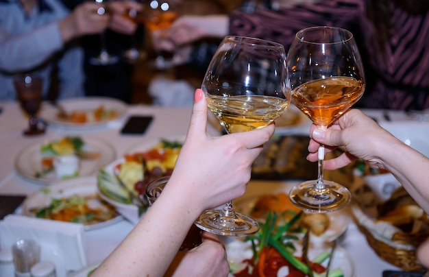 Brindisi alla tavola delle feste. Le mani della donna che tengono gli occhiali con bevande alcoliche, primo piano. Amici che tintinnano i bicchieri di vino.