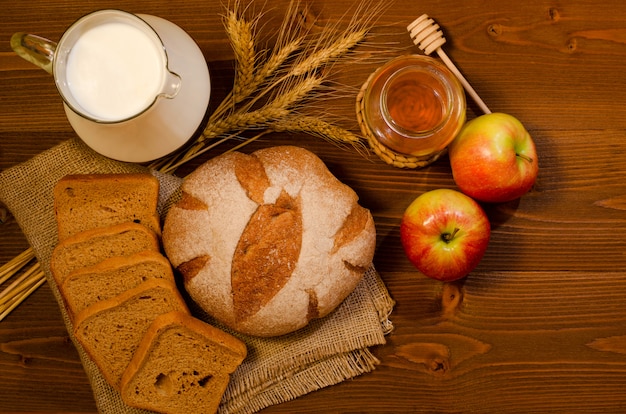 Brocca con latte, spighette, pane di segale, miele e mele su un tavolo di legno, vista dall'alto, spazio per il testo