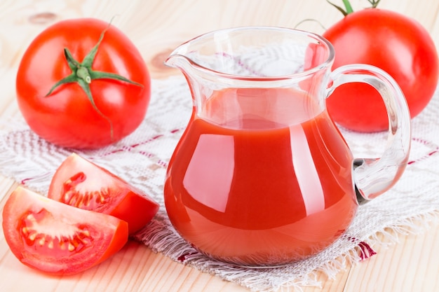 Brocca di succo di pomodoro fresco gustoso sdraiato sul tavolo di legno