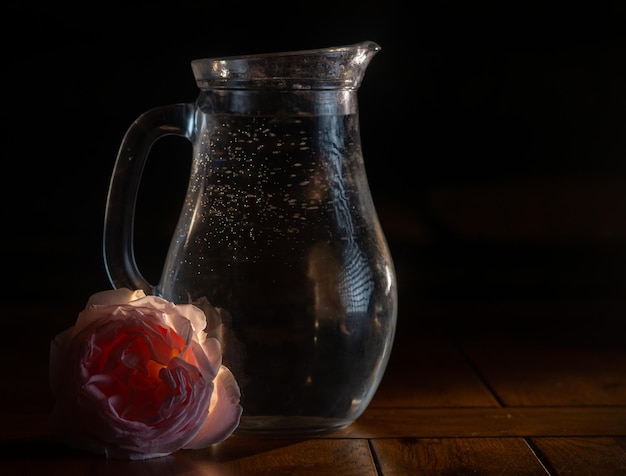 Brocca di vetro con acqua su fondo scuro con una rosa