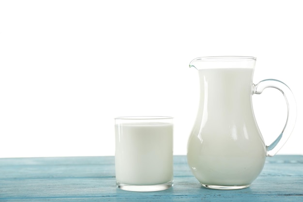 Brocca e bicchiere di latte sul tavolo di legno su sfondo bianco