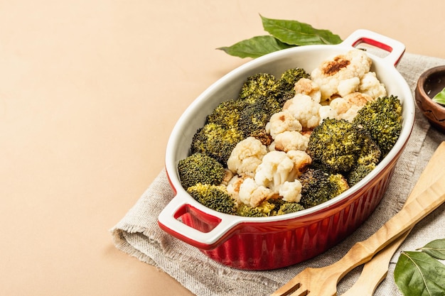 Broccoli e cavolfiori al forno. Posate in legno, foglie di alloro fresche, pepe verde in grani. Concetto di cibo sano, sfondo beige chiaro, copia spazio