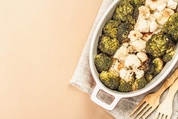 Broccoli e cavolfiori al forno. Posate in legno, foglie di alloro fresche, pepe verde in grani. Concetto di cibo sano, sfondo beige chiaro, vista dall'alto