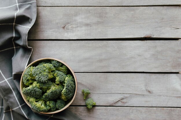 Broccoli freschi verdi nella ciotola su fondo di legno, tovagliolo grigio. Concetto di mangiare sano.