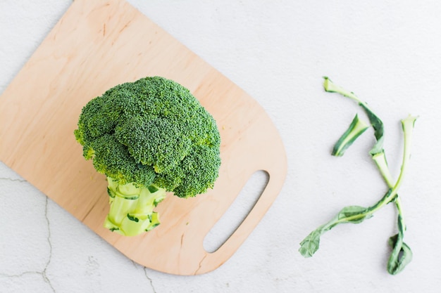 Broccoli interi crudi su un tagliere su un tavolo leggero Cucinare cibi vegetariani sani