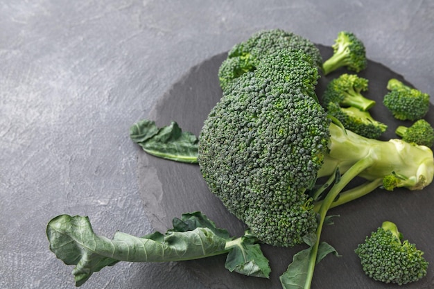 Broccoli interi e tagliati su piastra rustica in pietra ardesia. Cucinare cibi sani su sfondo grigio con spazio di copia. Verdure biologiche per i pasti di tutti i giorni