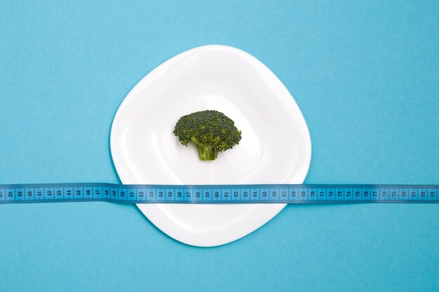 Broccoli su un piatto bianco e nastro di misurazione blu su sfondo blu