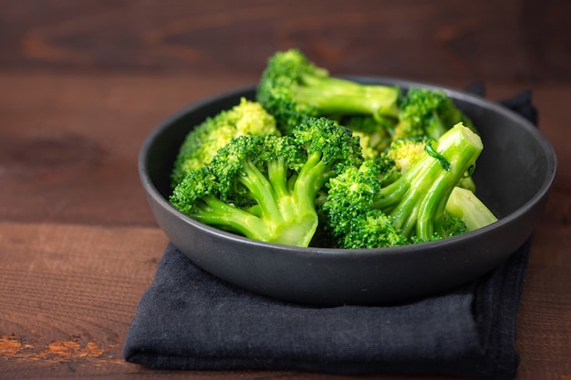 Broccoli verdi freschi sulla banda nera sopra fondo di legno marrone.