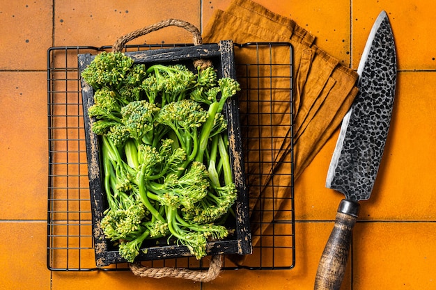 Broccolini verdi crudi in un vassoio di legno Sfondo arancione Vista dall'alto