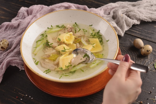 Brodo di pollo con carne, verdure e cipolle verdi. In un piatto bianco su un tavolo di legno