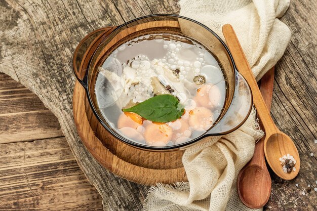 Brodo di pollo trasparente. Zuppa chiara a basso contenuto di grassi con carote, verdure e spezie. Piatto caldo, posate, vecchio fondo in legno, vista dall'alto