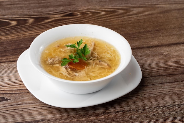 Brodo di zuppa di pollo gustoso con noodles carne di pollo aneto e prezzemolo in una ciotola bianca isolata su sfondo di legno Menu pasto sano