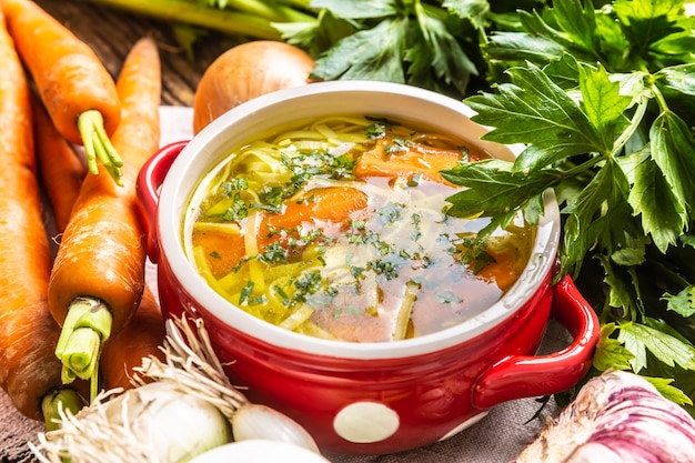 Brodo di zuppa di pollo o verdura in una ciotola vintage con tagliatelle fatte in casa carota cipolla sedano erbe aglio e verdure fresche.