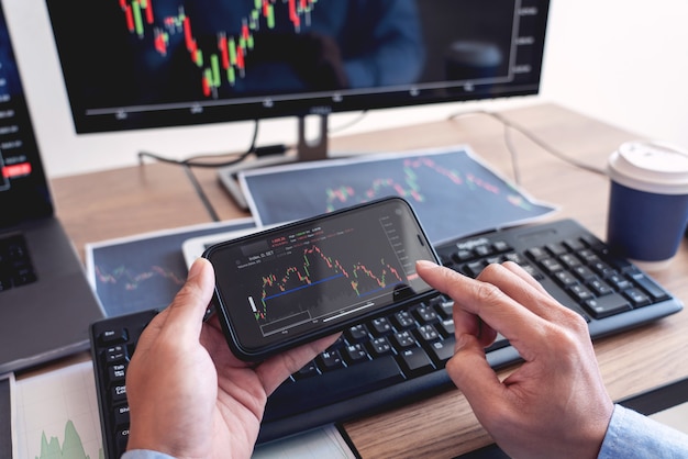 Broker di uomo d'affari analizzando grafici di dati finanziari e report sullo schermo