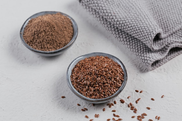 Brown semi di lino e semi di lino macinati o schiacciati o semi di lino in una piccola ciotola su un grigio chiaro.