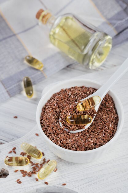 Brown semi di lino o semi di lino in una piccola ciotola e capsule di gelatina con olio di omega su un legno bianco.