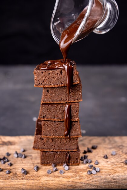 Brownie al cacao versando con cioccolato fondente fuso su un piatto bianco.