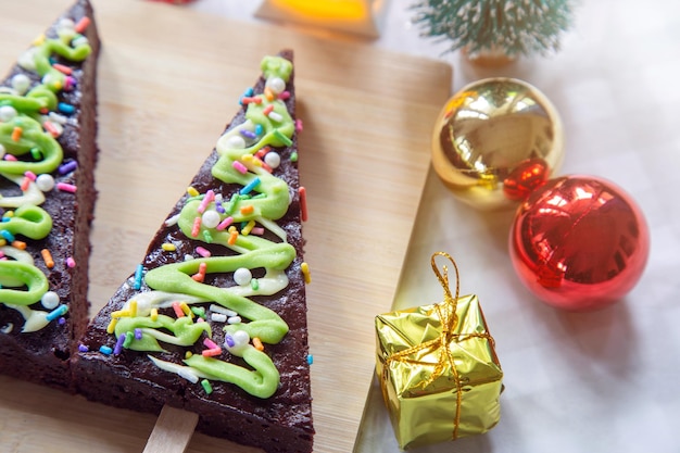 Brownies al cioccolato a forma di alberi di Natale con glassa verde su un tagliere di legno con una palla e decorazione per il festival di Natale