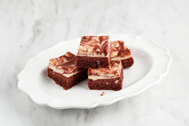 Brownies di formaggio cremoso di velluto rosso su piastra in ceramica bianca, isolata