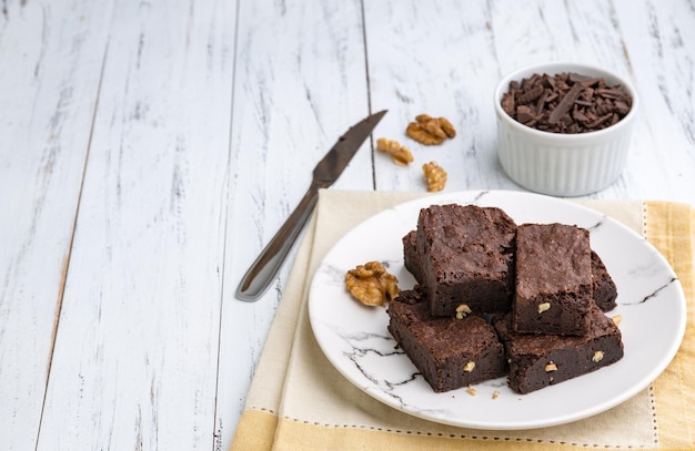 Brownies su un piatto con pezzi di cioccolato e noci su tavolo di legno bianco con spazio per le copie