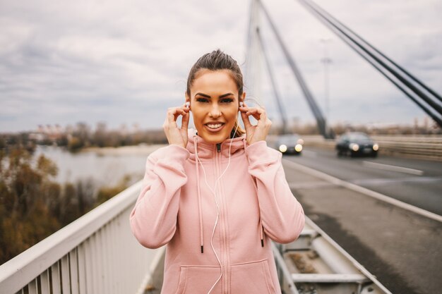 Bruna che mette gli auricolari e si prepara per correre sul ponte con tempo nuvoloso