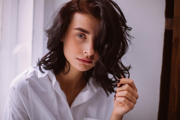 Bruna con i capelli ricci che indossa una camicia bianca seduta sull'elaborazione di foto d'epoca della finestra