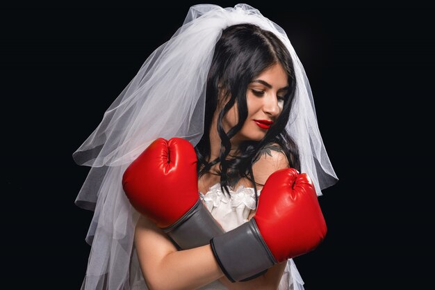 bruna con rossetto rosso in abito da sposa velo e guantoni da boxe