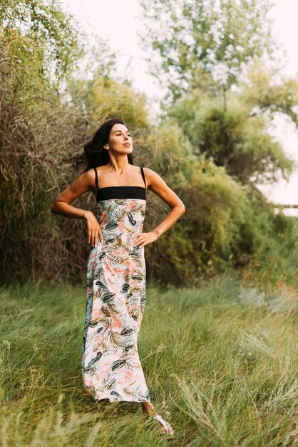 bruna in un elegante abito estivo e cappello di paglia sotto i raggi del sole sulla passeggiata nella natura