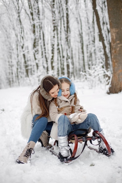 Bruna madre e figlia seduta su una slitta nella foresta invernale