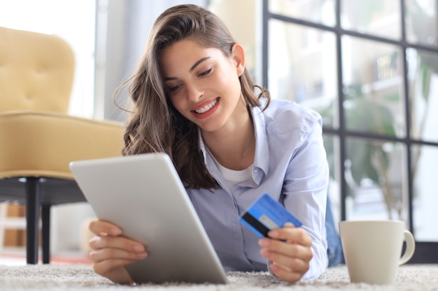 Bruna naturale felice utilizzando carta di credito e laptop in soggiorno.