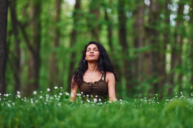 Bruna positiva in abiti casual che medita nella foresta durante il giorno